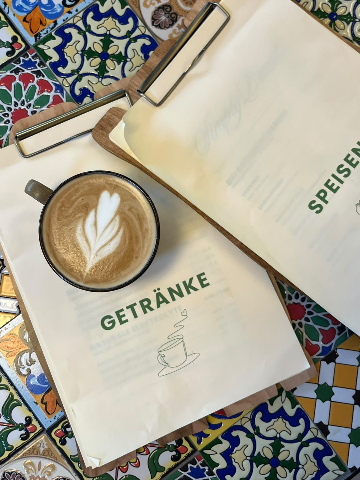 Cappuccino mit Latte-Art auf der GETRÄNKE-Karte über bunten Fliesen