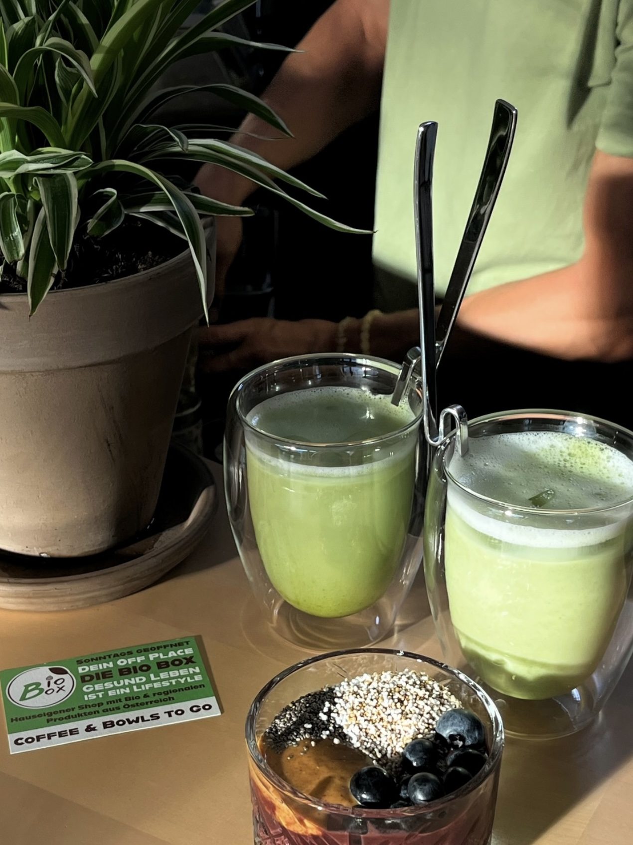 Zwei Matcha-Lattes und ein Smoothie-Bowl auf hellem Tisch